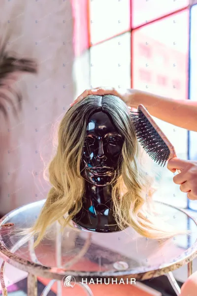 A wavy ombre blonde wig on a black mannequin head, a brush touching the hair