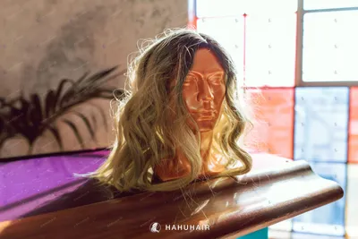 A wavy blonde wig on a copper-coloured mannequin head by a window