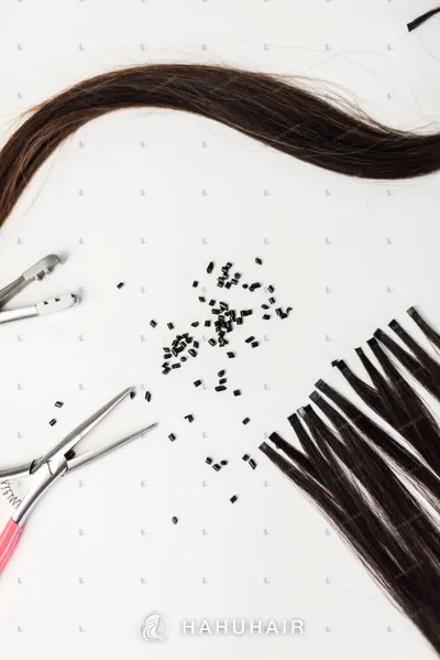 Dark brown hair strands with keratin beads and pliers on a white background