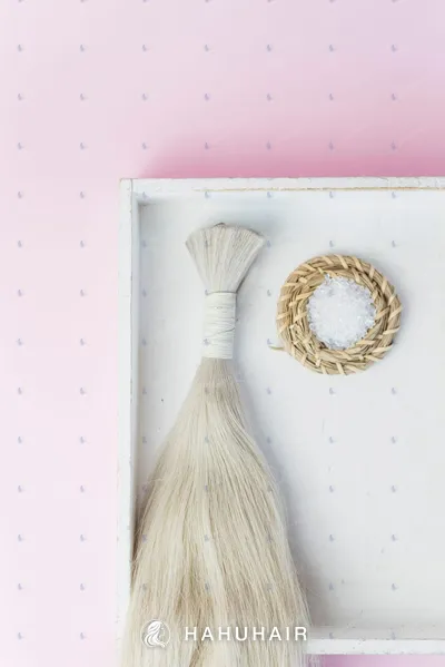 A tied bundle of long blonde bulk hair in a white tray beside a small round decoration