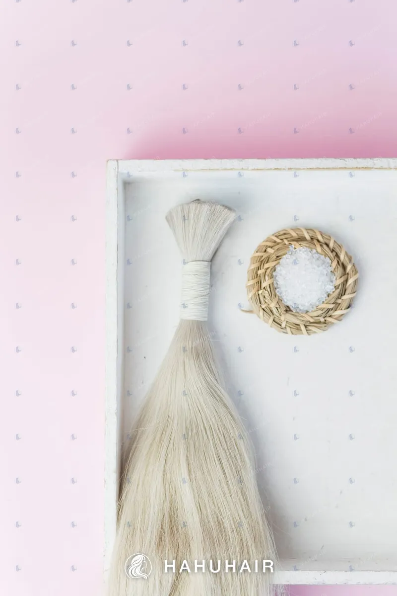 A tied bundle of long blonde bulk hair in a white tray beside a small round decoration