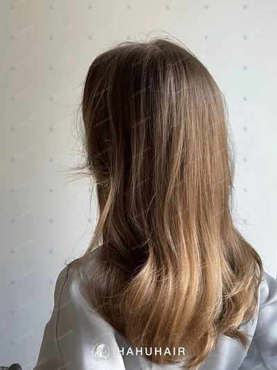 Long straight brown hair with lighter ends seen from behind, white wall