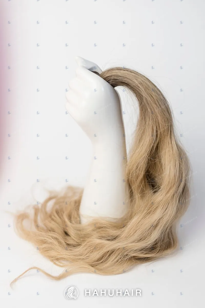 A long wavy honey-blonde hair tress held up by a white mannequin hand