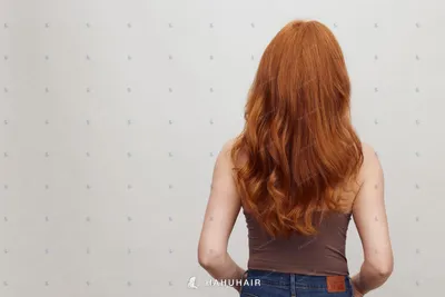 Long wavy copper-red hair seen from behind against a plain wall