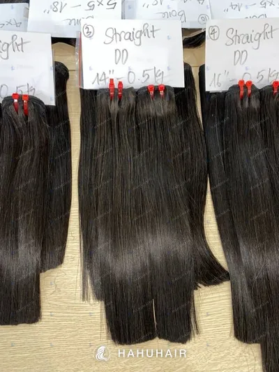 Natural straight black hair wefts on a table with handwritten length and grade labels