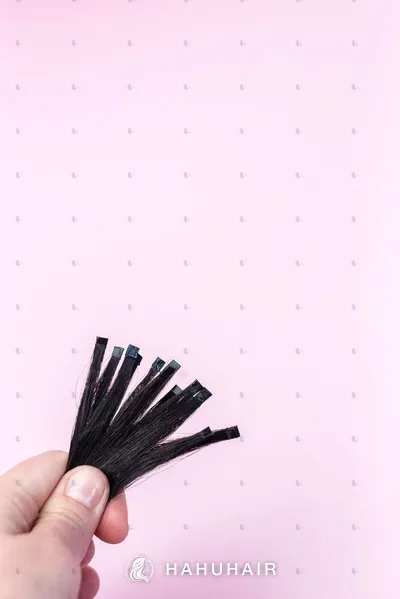 A hand holding a few thin black hair strips against a pink background