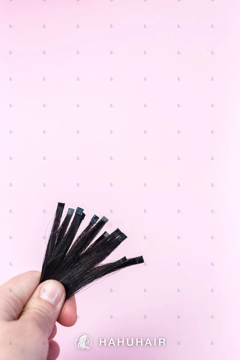 A hand holding a few thin black hair strips against a pink background