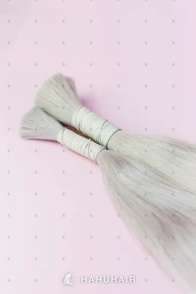 Two tied bundles of ash-grey blonde hair on a pink background