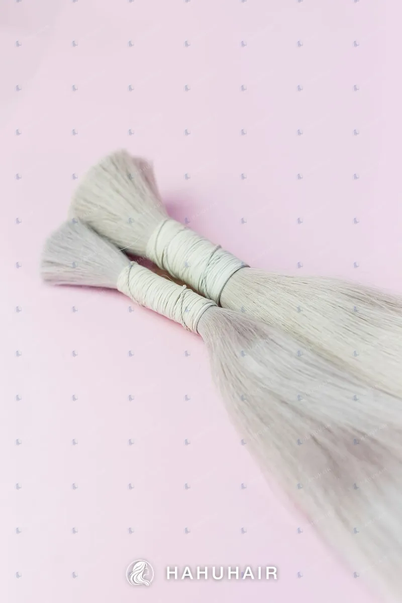Two tied bundles of ash-grey blonde hair on a pink background