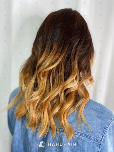Wavy hair fading from dark brown roots to golden blonde ends, seen from behind