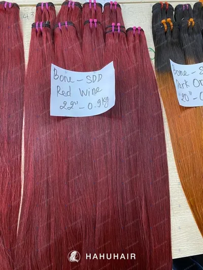 Bone straight red wine hair wefts on a table with handwritten length and grade labels