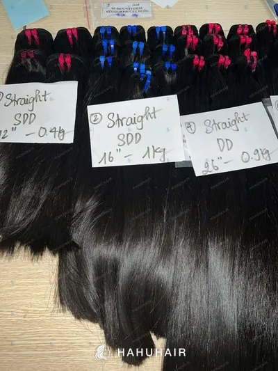 Natural straight black hair wefts on a table with handwritten length and grade labels